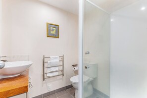 Um banheiro moderno com uma pia grande branca, box de vidro e vaso sanitário.