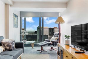 Een moderne woonkamer met een bank, fauteuil, poef, salontafel en een televisie op een houten kast.
