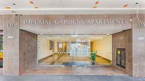 The entrance to Imperial Gardens Apartments, featuring a tiled facade, a glass door entrance, and a visible plant in the center. - Zodiak Stays: Cozy CBD 2BR Near Top Dining Spots (Auckland)