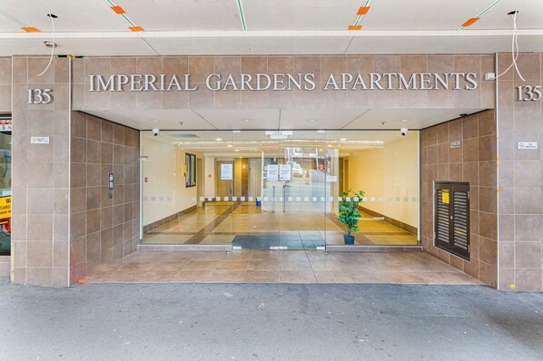 The entrance to Imperial Gardens Apartments, featuring a tiled facade, a glass door entrance, and a visible plant in the center. - Zodiak Stays: Cozy CBD 2BR Near Top Dining Spots (Auckland)
