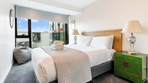 A hotel room with a bed, bedside lamps, a green nightstand, and a view of the outside. - Zodiak Stays: Cozy CBD 2BR Near Top Dining Spots (Auckland)