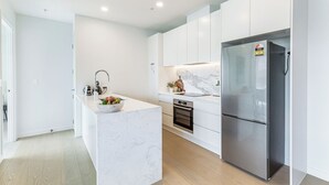 Eine moderne Küche mit weißen Schränken, einer Marmorarbeitsplatte, einem Edelstahlkühlschrank und einem Backofen.
