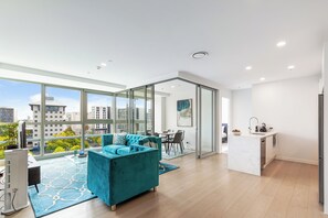 Un apartamento moderno con un amplio ventanal, un sofá azul, una zona de cocina y una mesa de comedor.