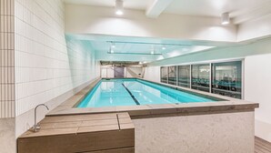 Ein Innenpool mit deutlich abgetrennten Bahnen, einer Holzterrasse und einer Glaswand auf einer Seite.