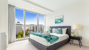 Ein modernes Schlafzimmer mit einem großen Bett, einem Nachttisch und Blick auf die Stadt durch große Fenster.
