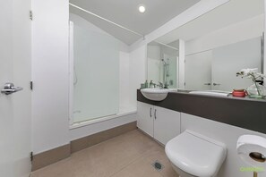 Een moderne badkamer met een douchecabine van glas, een wit toilet en een wastafel met een wastafel en spiegel.