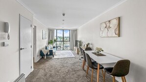 A modern hotel room with a dining area, a view through the window, and a radiator on the floor. - 2BR Newmarket Retreat near Broadway: Zodiak Stays (Auckland)