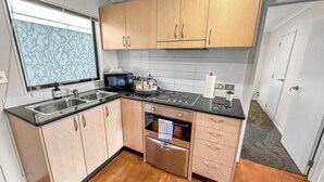 A modern kitchen with wooden cabinets, stainless steel appliances, and a black countertop. - 2BR Newmarket Retreat near Broadway: Zodiak Stays (Auckland)