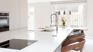 Une cuisine moderne dotée d’un grand îlot central, de meubles blancs et offrant une vue sur l’extérieur.