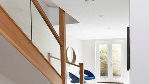 Un intérieur moderne avec un escalier en bois, une chaise bleue et une porte donnant sur un espace extérieur.