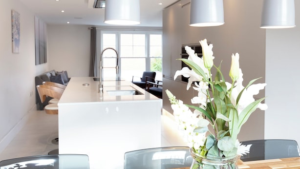 Une cuisine moderne dotée d’un îlot central, de luminaires suspendus et d’un coin repas avec une table en verre.