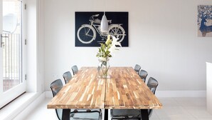 Un coin repas avec une table en bois, des chaises, un vase de fleurs, un tableau sur le thème du vélo et un tableau représentant la silhouette d’un arbre.