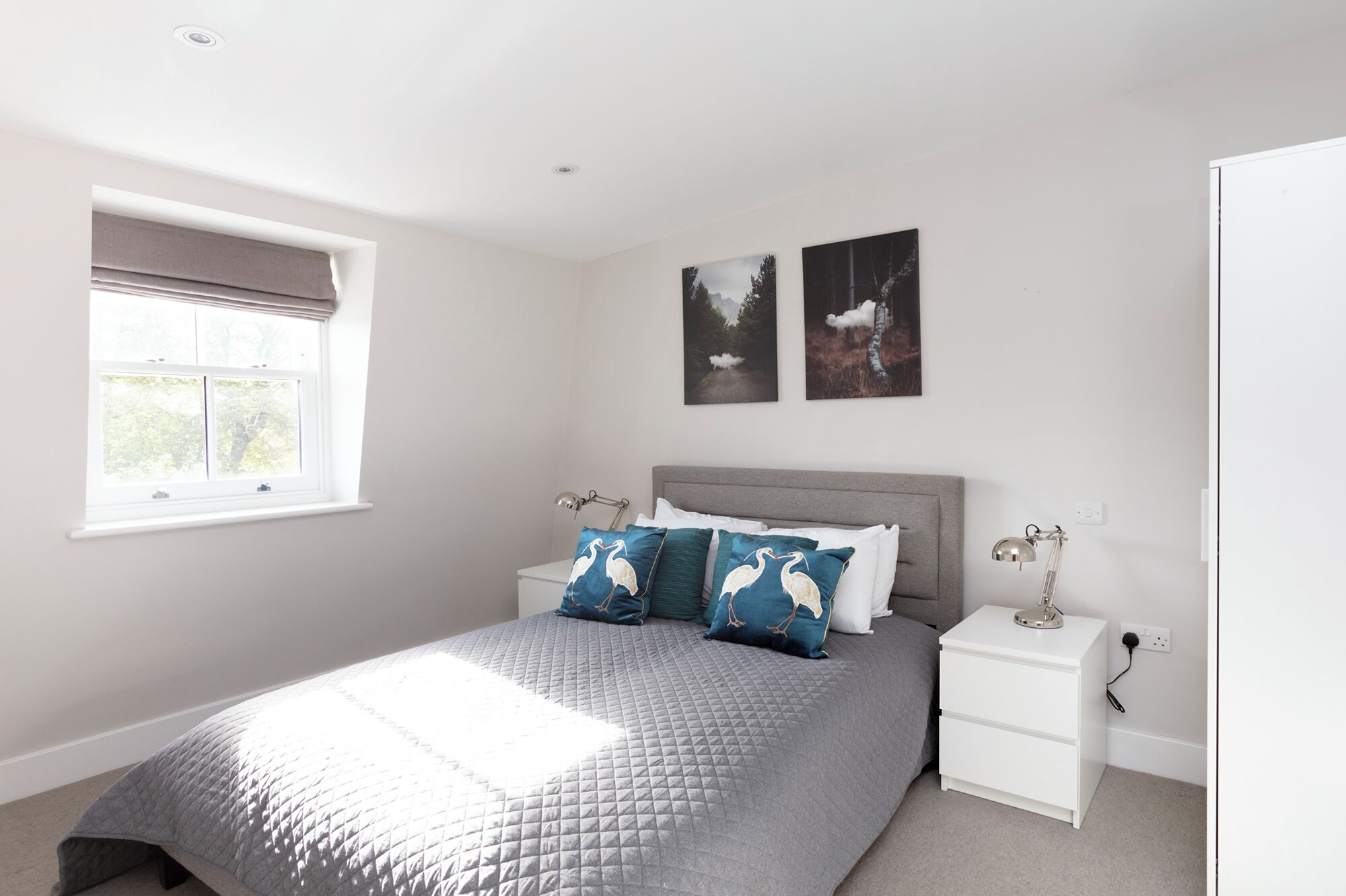 Une chambre à coucher comprenant un lit, deux tables de chevet, une fenêtre et deux tableaux accrochés au mur.