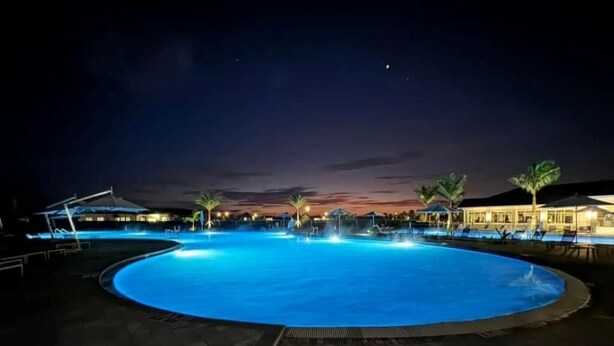 A large, circular swimming pool at night with surrounding buildings and palm trees. - Cozy 2-bedroom condo with WiFi, fitness room in charming Babcock Ranch Florida.  (Punta Gorda)