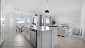 A modern kitchen with a central island, dining area with chairs, and a living space with a sofa and TV. - Cozy 2-bedroom condo with WiFi, fitness room in charming Babcock Ranch Florida.  (Punta Gorda)