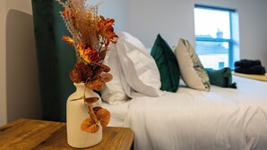 Ein Hotelzimmer mit Bett, Kissen, einer Vase mit getrockneten Blumen und einem Fenster mit Blick.