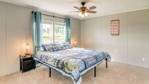Ein Schlafzimmer mit einem Bett, einem Deckenventilator, einem Nachttisch mit Lampe und einem Fenster mit Vorhängen.