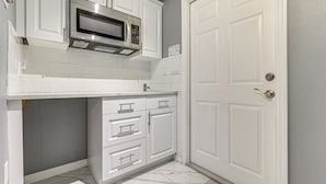A compact kitchen with white cabinetry, a built-in microwave, and a door with a handle. - 10 Mi to Adventure Island: Home w/ Fenced Yard! (Lutz)