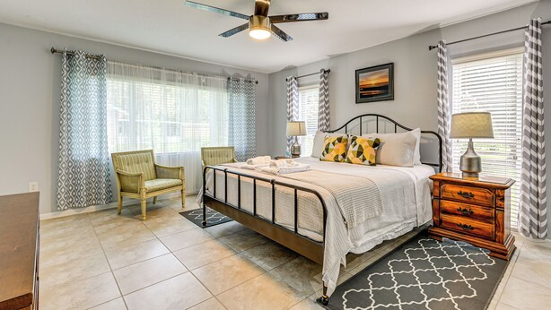 A bedroom with a bed, a chair, a nightstand, a lamp, and a ceiling fan. - 10 Mi to Adventure Island: Home w/ Fenced Yard! (Lutz)