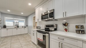 A modern kitchen with white cabinets, stainless steel appliances, and a window with blinds. - 10 Mi to Adventure Island: Home w/ Fenced Yard! (Lutz)