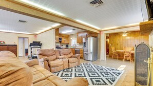 Een ruime woonkamer met een grote bruine hoekbank, een vloerkleed met patroon en een keuken voorzien van houten kastjes en moderne apparatuur.