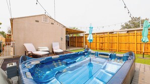 Een achtertuin met een jacuzzi, twee loungestoelen en een houten omheining.