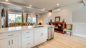 Una cocina moderna con una isla grande, armarios blancos y lavavajillas. Hay un área de comedor con un sofá y una chimenea.