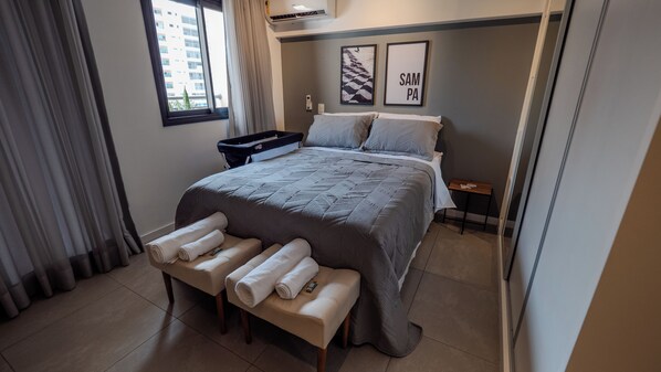 Ein Hotelzimmer mit einem großen Bett, einer Bank mit Handtüchern, einem kleinen Tisch und einem Fenster mit Vorhängen.