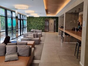 Eine moderne Hotellobby mit einer langen Rezeption, einer Sitzecke mit Sofas und einer grünen Wand mit Pflanzen.