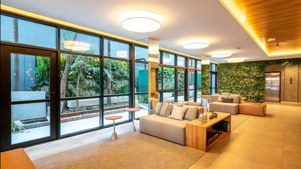 A modern lobby with large windows, a sofa, a coffee table, and a green wall.