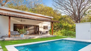 Une maison moderne dotée d’une piscine, d’un espace salon extérieur et d’un toit de chaume.