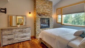 Un dormitorio con chimenea de piedra, cómoda de madera y una cama grande con vista al exterior.