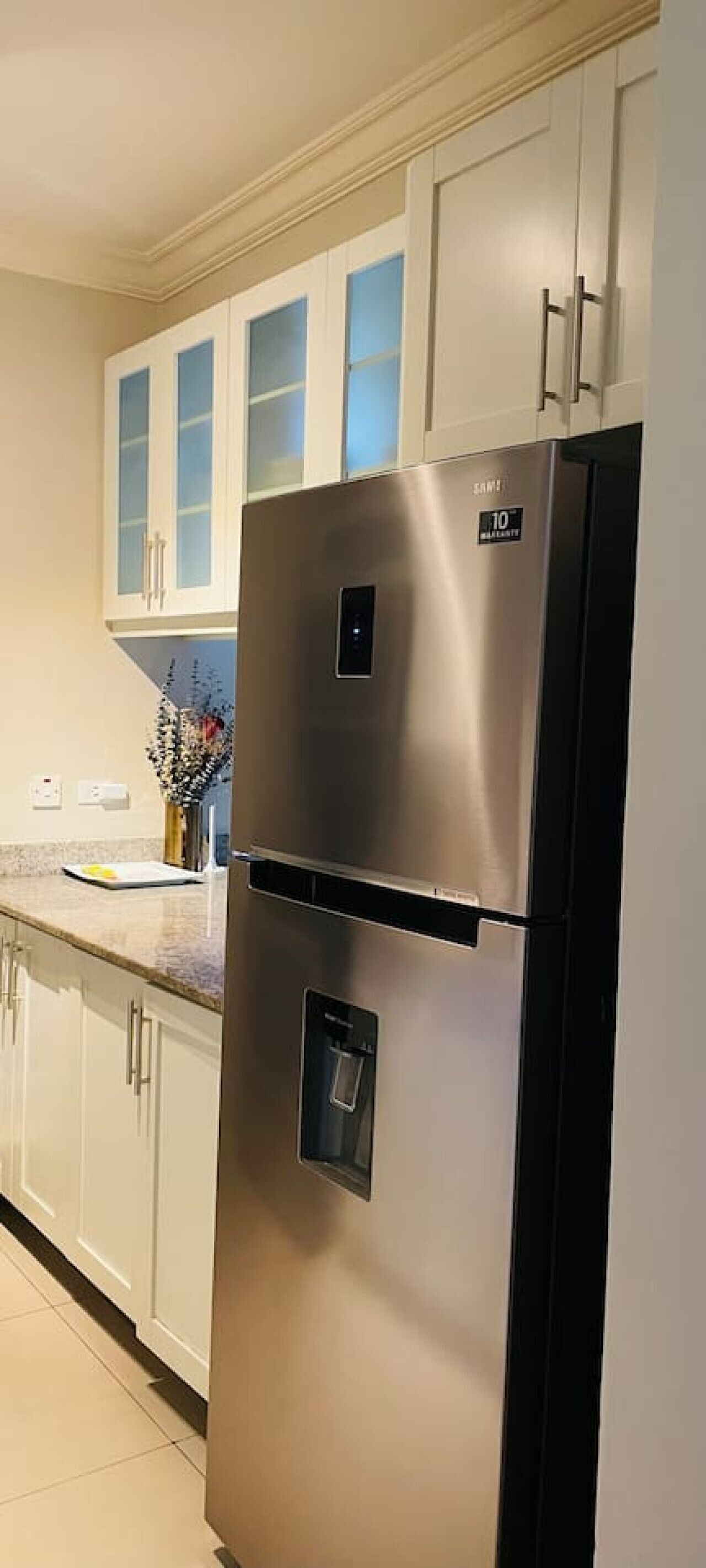 A stainless steel refrigerator with a water dispenser, white cabinets, and a kitchen counter.
