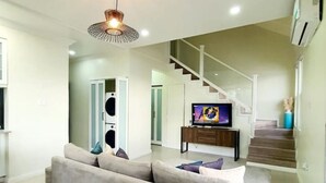 Ein modernes Wohnzimmer mit einem beigen Sofa, einem Flachbildfernseher und einer Treppe, die zu einer oberen Etage führt.