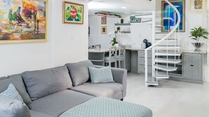 A modern living room with a grey sofa, a staircase, and various framed artworks on the walls. - Choose To Be Happy @ The Seville #E3 [2-Bedroom] (Kingston)