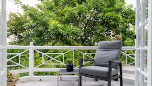 A balcony with a grey chair, a small table, and potted plants. - Choose To Be Happy @ The Seville #E3 [2-Bedroom] (Kingston)