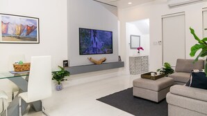 A modern living room with a glass coffee table, a sofa, and a TV mounted on the wall. - Choose To Be Happy @ The GAIA [2-Bedroom w/ Pool] (Kingston)