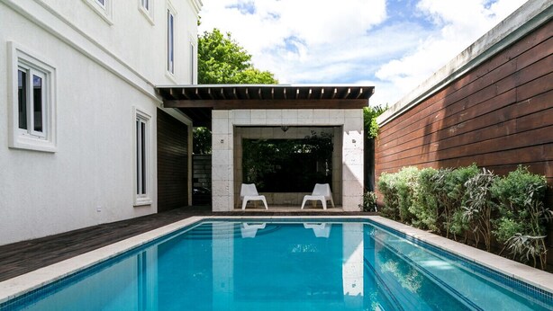 A swimming pool with two white lounge chairs, a pergola, and a white building with windows. - Choose To Be Happy @ The GAIA [2-Bedroom w/ Pool] (Kingston)