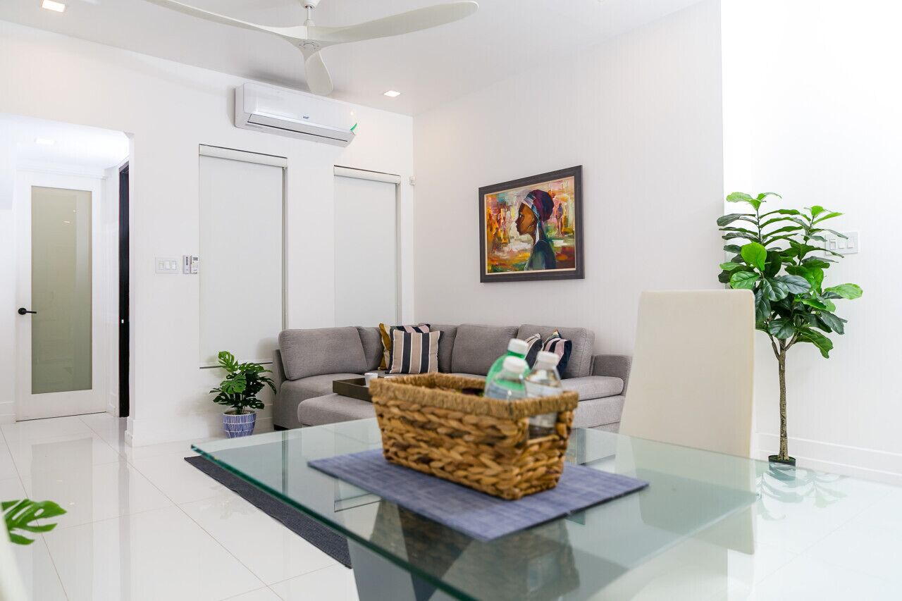 Un salon moderne avec une table basse en verre, un canapé gris, un tableau encadré et une plante en pot.