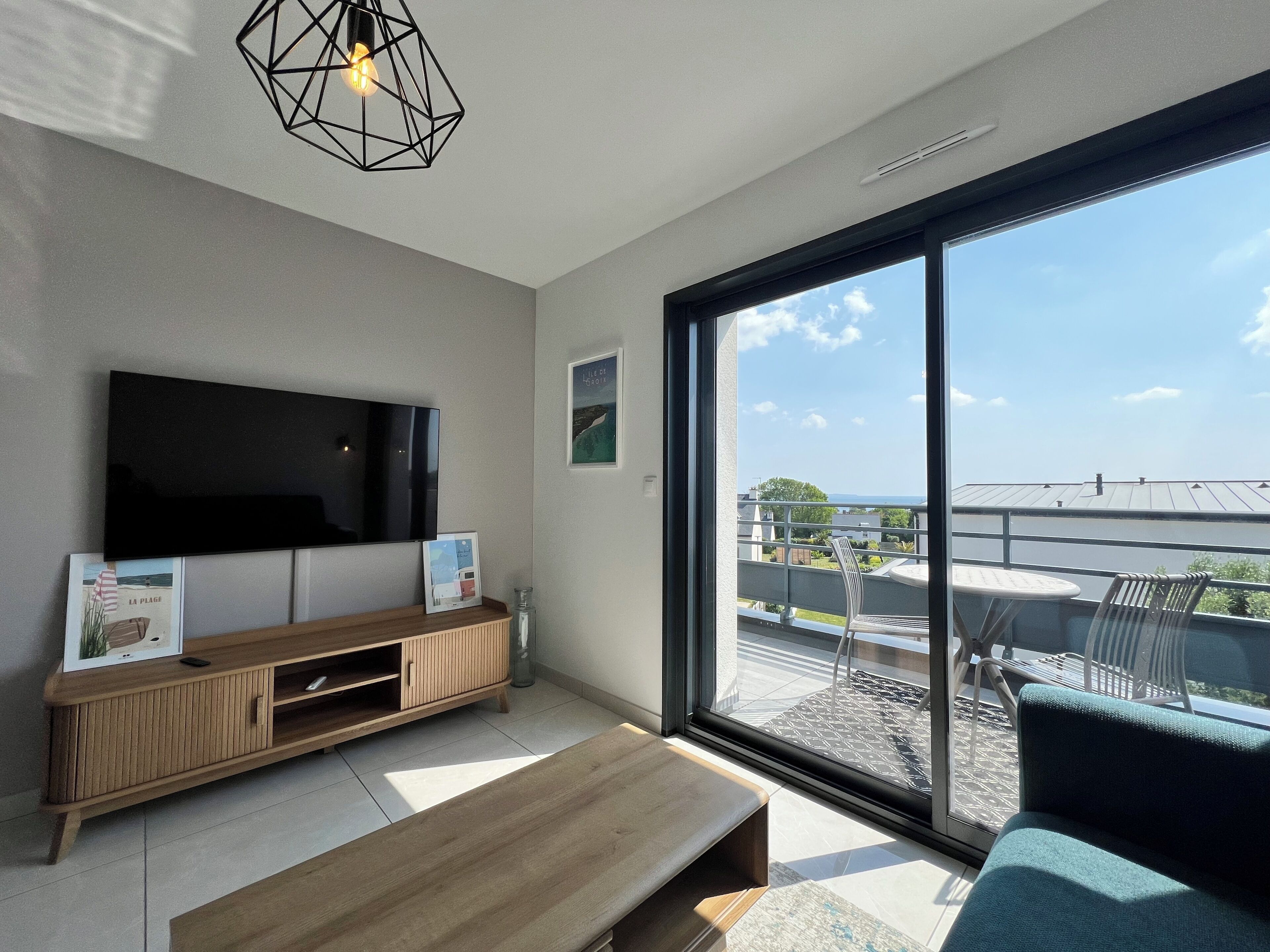 Un salon moderne doté d’un grand téléviseur, d’un meuble de rangement en bois, d’un banc et d’un balcon aménagé avec du mobilier d’extérieur.