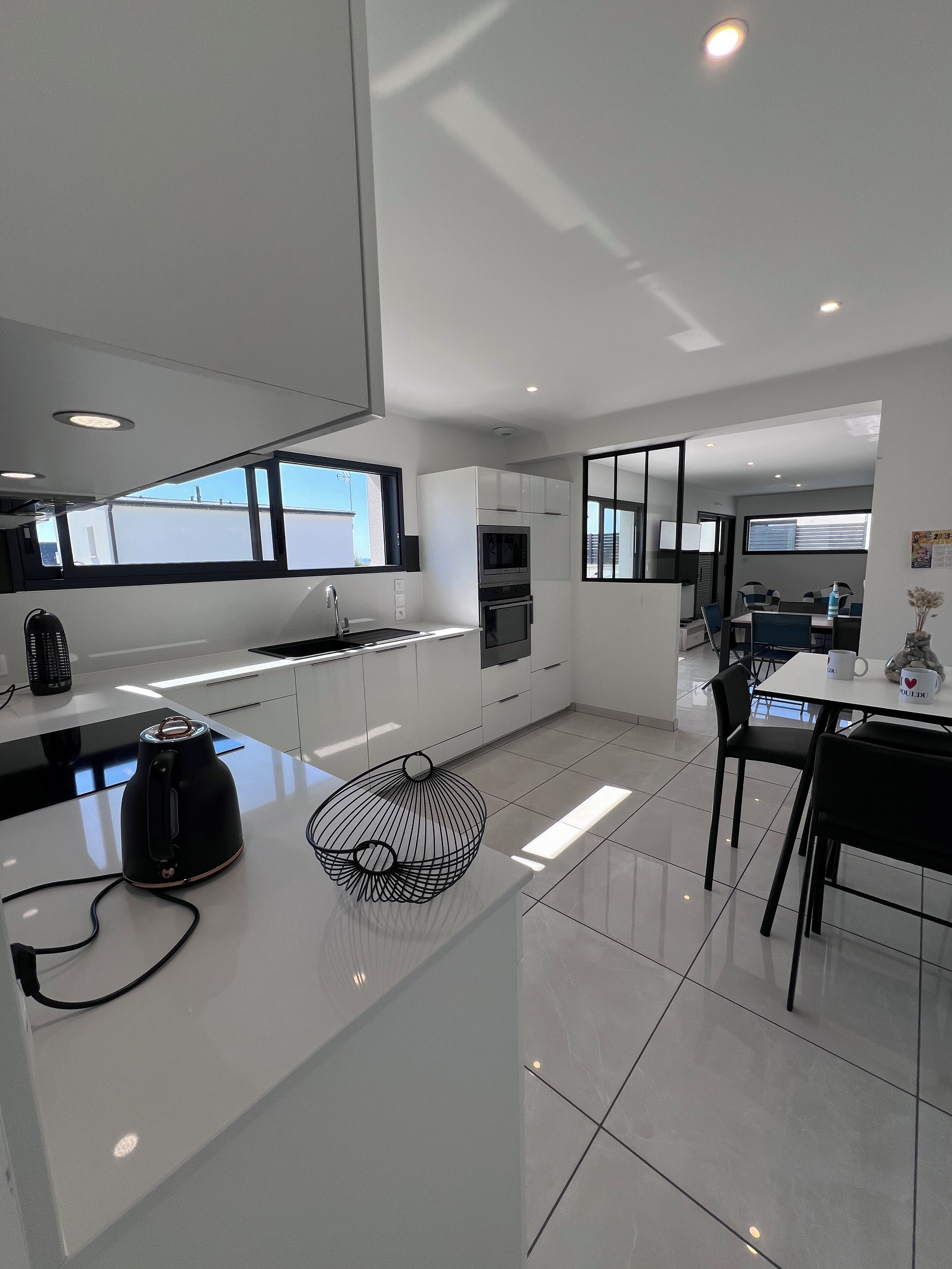 Een moderne keuken met witte kastjes, een zwarte waterkoker en een decoratieve metalen kom op het aanrecht.