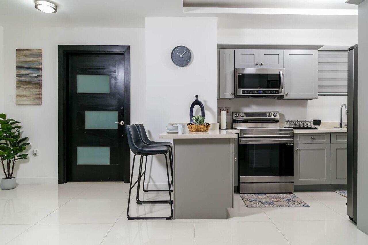 Una cocina moderna con puerta negra, electrodomésticos de acero inoxidable y una pequeña isla con taburetes de bar.