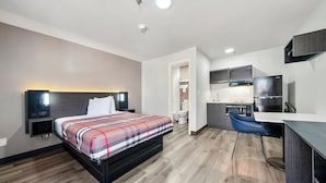 Una habitación de hotel moderna con cama, mesita de noche y una zona de kitchenette.