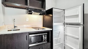 Una cocina compacta con microondas integrado, un lavamanos y un refrigerador de dos puertas.
