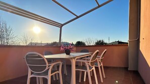 A balcony with a table and chairs, a potted plant, and a view of the sky and buildings.