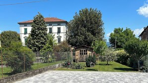 A paved courtyard with a stone floor, surrounded by a fence, and featuring a large building with a red roof in the background.