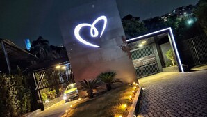 Entrada de un edificio con una instalación de luces con forma de corazón, senderos empedrados y un pequeño jardín con plantas.
