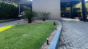 Fachada de edificio con logotipo en forma de corazón, paseo empedrado y vegetación.
