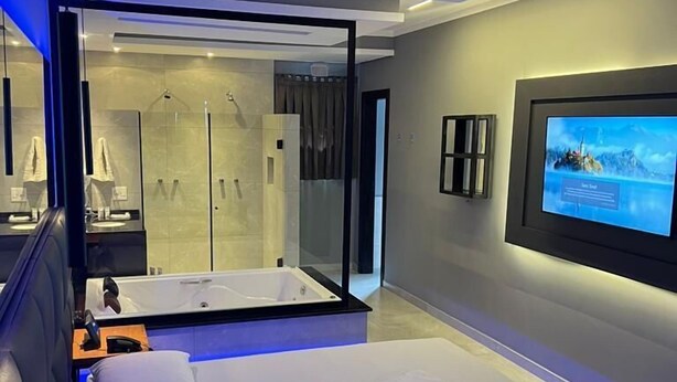 Un hotel moderno con una cama grande, un televisor montado en la pared y un baño visible a través de un separador de vidrio.