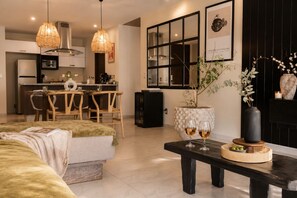 A modern living room with a sofa, dining table, and chairs, a kitchen in the background, and a decorative vase with flowers. - Wabi Sabi 3 BedRoom / Daily Clean (Guadalajara)